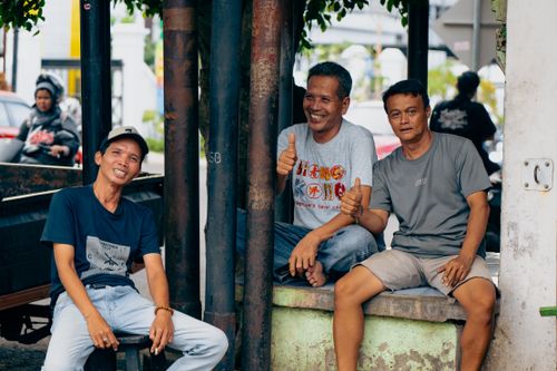 Free Three men smiling and giving thumbs up while sitting together on a street in Subang, Indonesia. Stock Photo