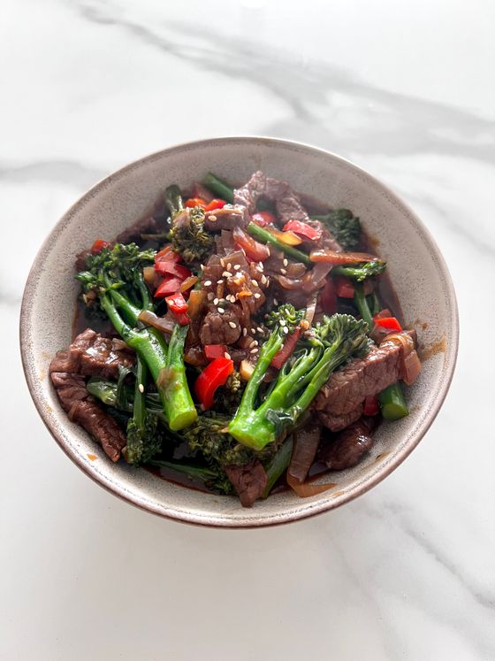Bowl of stir-fried beef strips with broccolini, red bell pepper, onion, glossy sauce and sesame