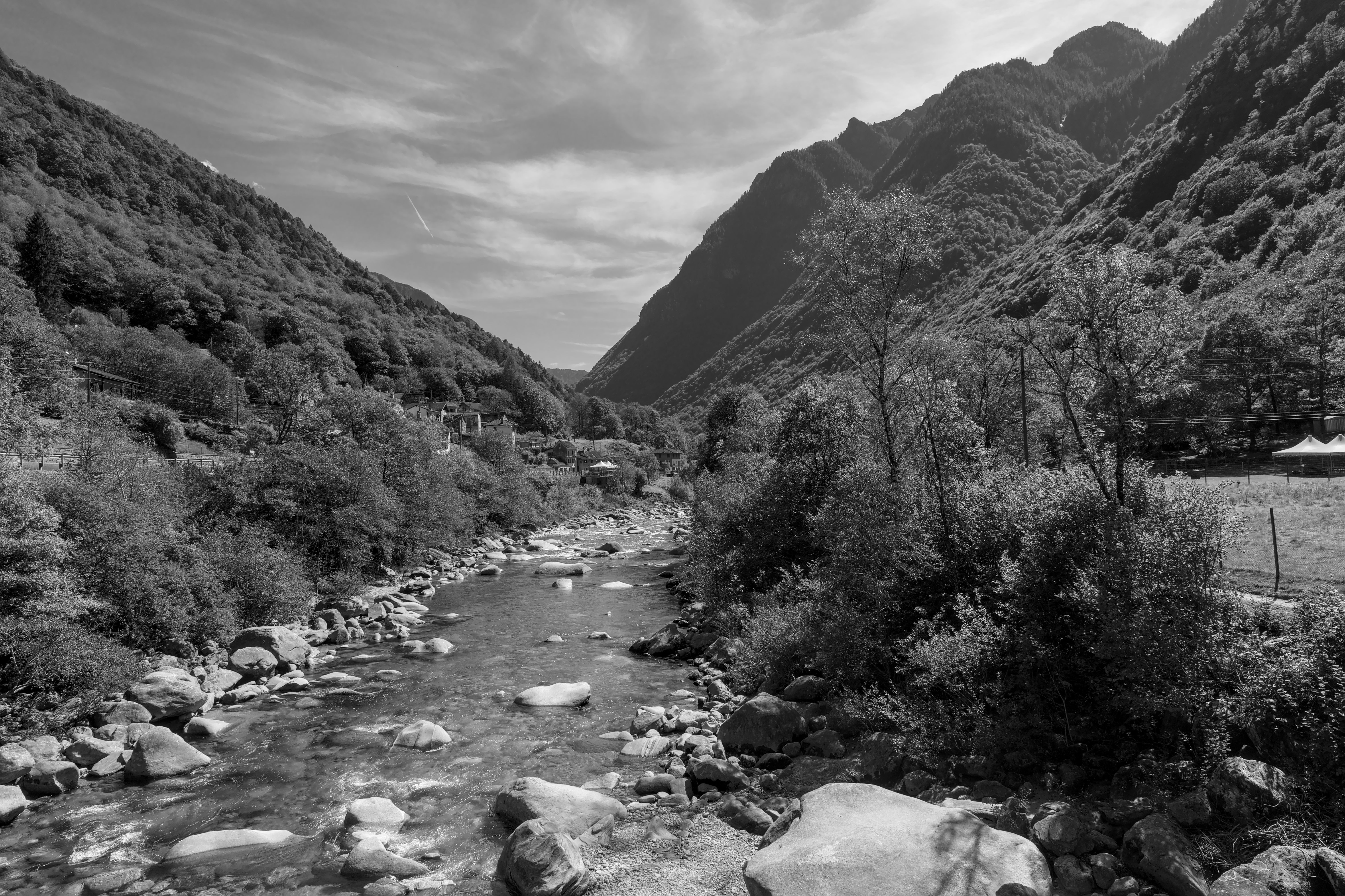 A tranquil view of Valle Verzasca's river flanked by lush greenery and mountainous terrain.
