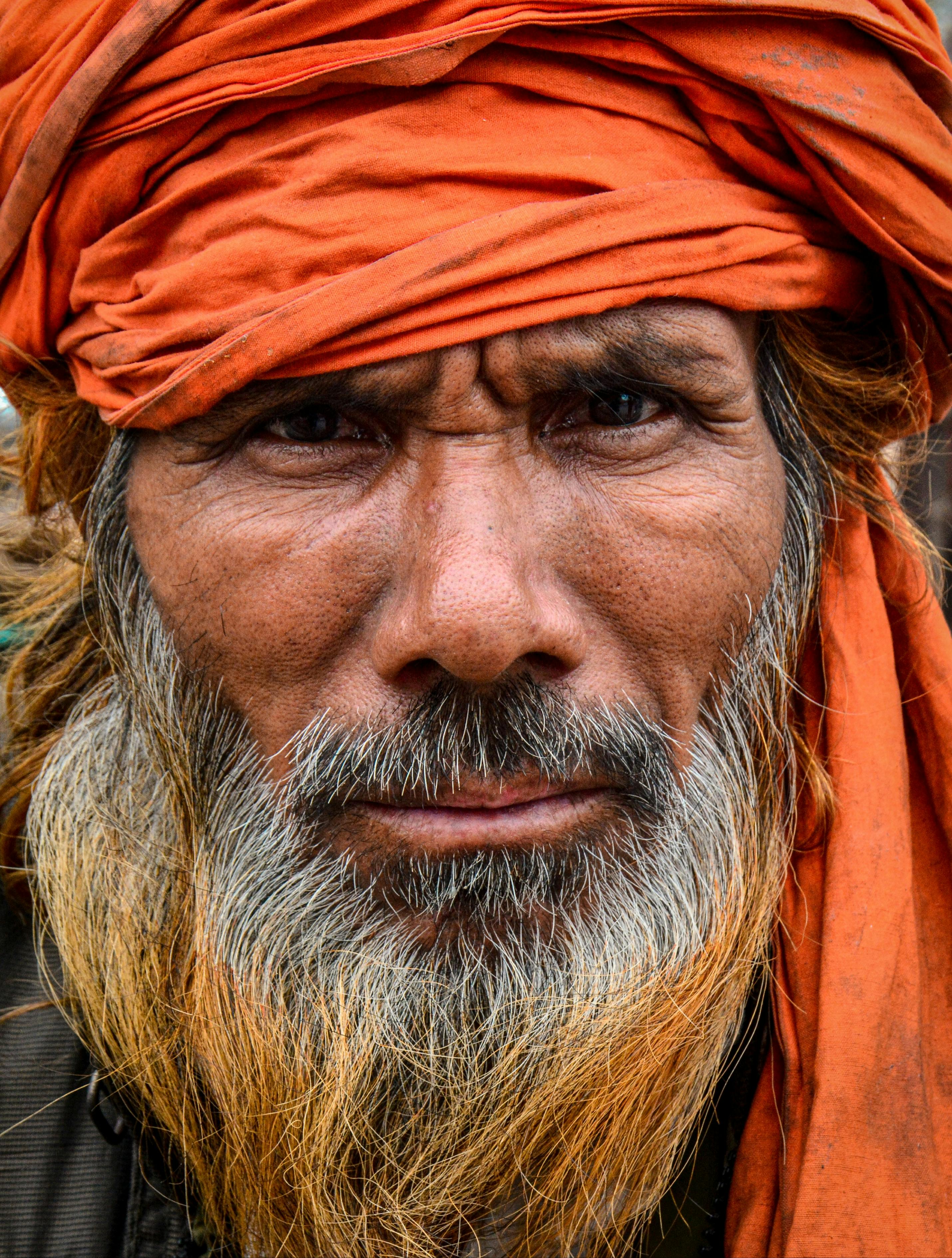 Gratis Nærbilde av en eldre mann i oransje turban, som viser frem hans intense blikk og værbitte ansiktstrekk. Arkivbilde