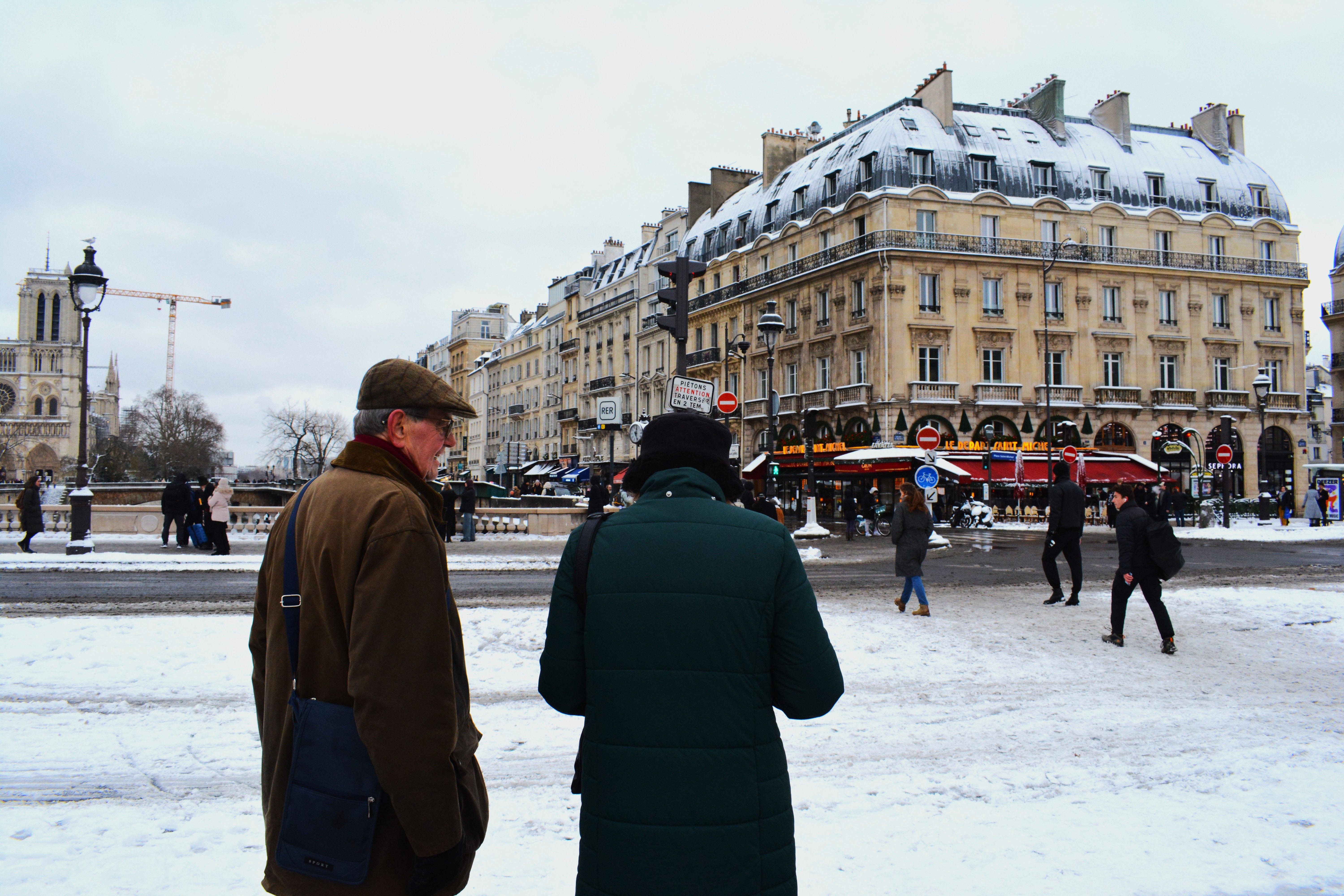 A Paris street near Notre Dame in winter, snow on the buildings and people walking