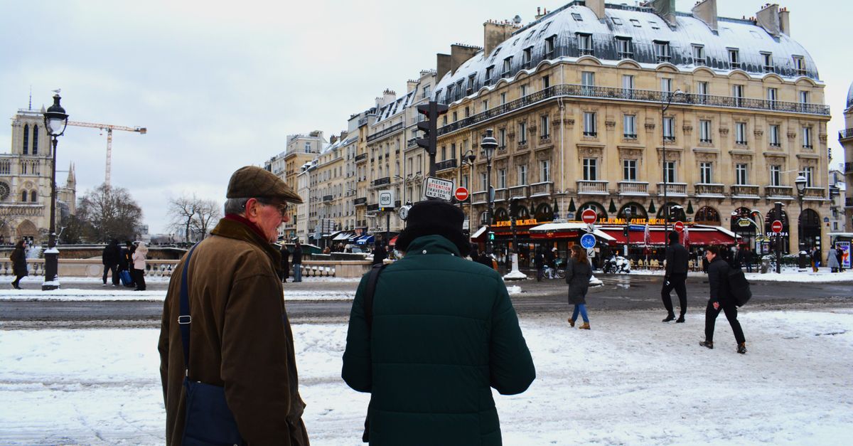 A Paris street near Notre Dame in winter, snow on the buildings and people walking