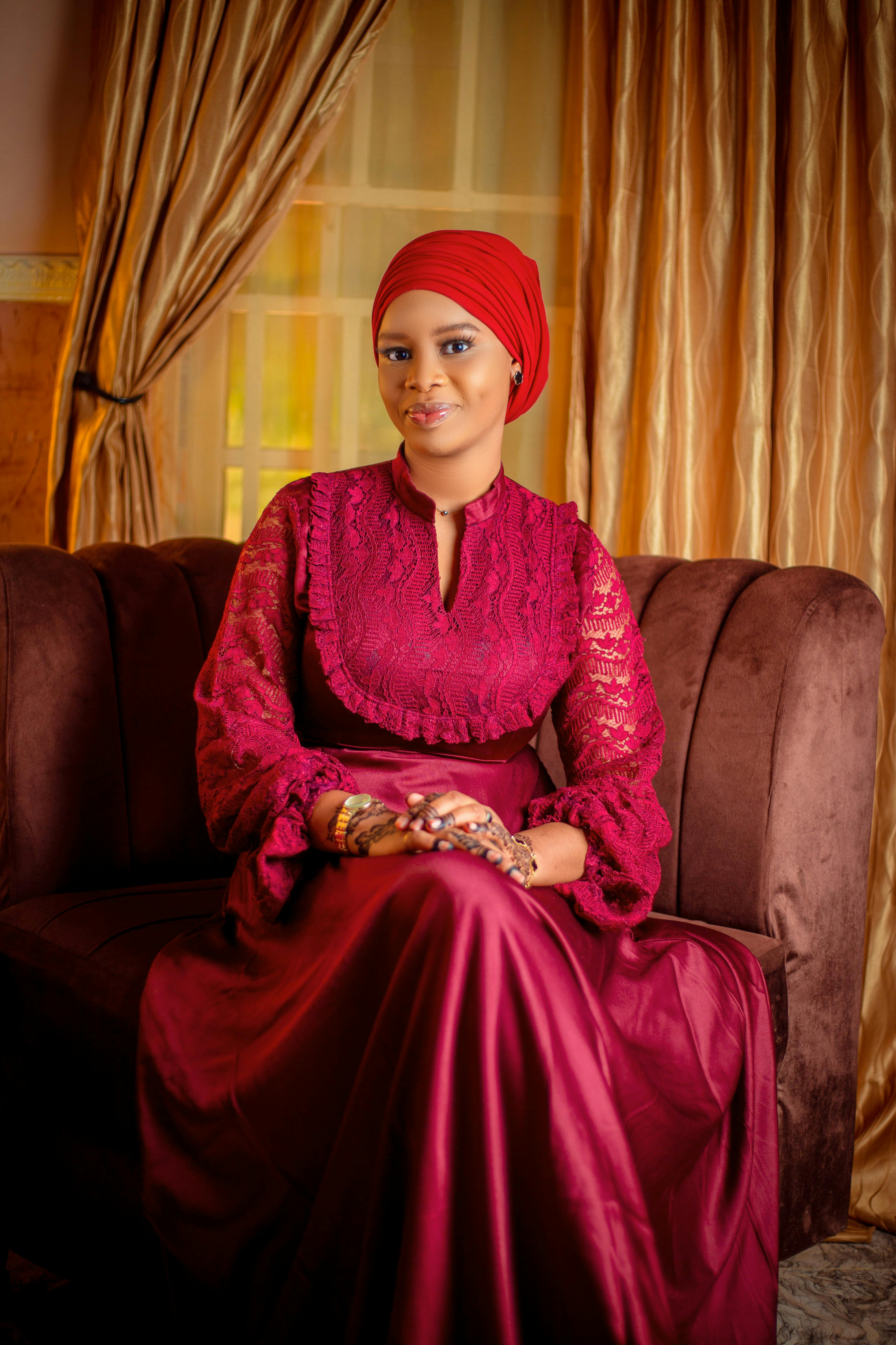 Zadarmo Žena v červených šatách a šatke na hlave elegantne sedí na pohovke a predvádza vyrovnanosť a štýl. Fotka z fotobanky