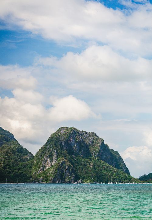 Free A beautiful island with lush green mountains and turquoise waters under a partly cloudy sky. Stock Photo