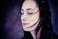 一位闭着眼睛的女子，在宁静的雪景中，发丝轻扬