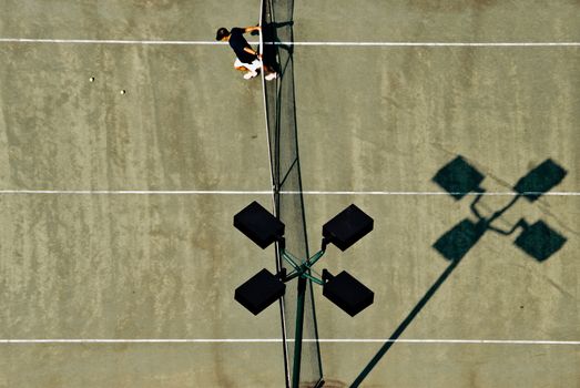 Top-down view of a tennis court on Hong Kong Island, featuring shadows and a solitary player.