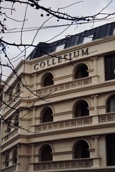 Neoclassical architecture of the Collesium building captured from street view with bare branches.