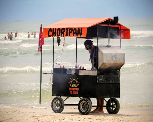 Free Vendor cooking at a Choripan cart on a lively beach scene. Stock Photo