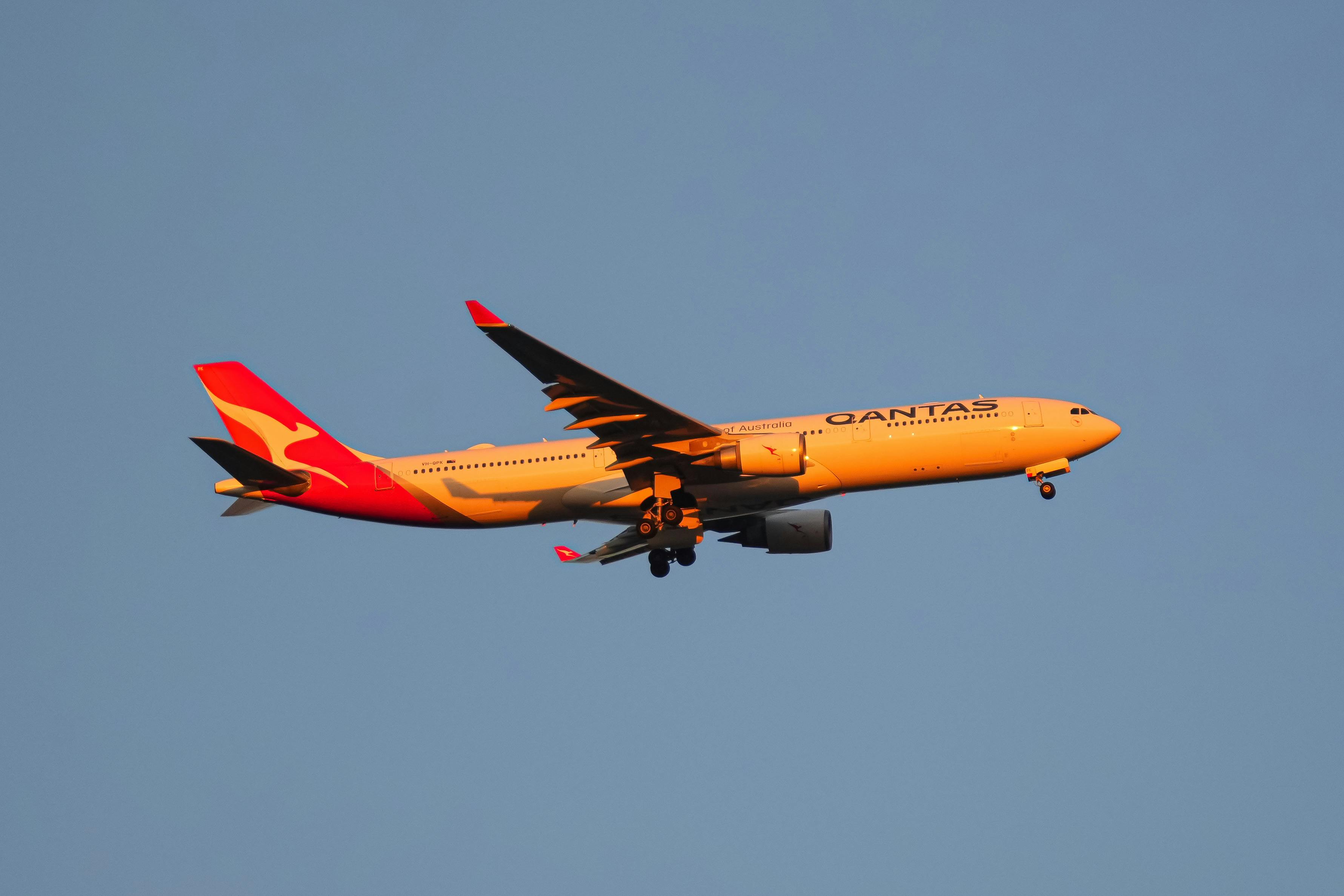 A vibrant Qantas passenger plane in flight against a clear blue sky during sunset.