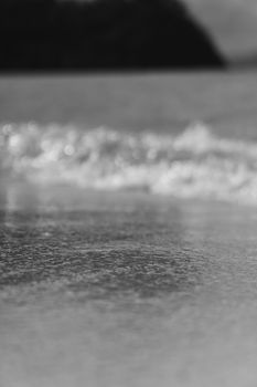 Monochrome image of ocean waves gently lapping onto a sandy beach, soft and peaceful.