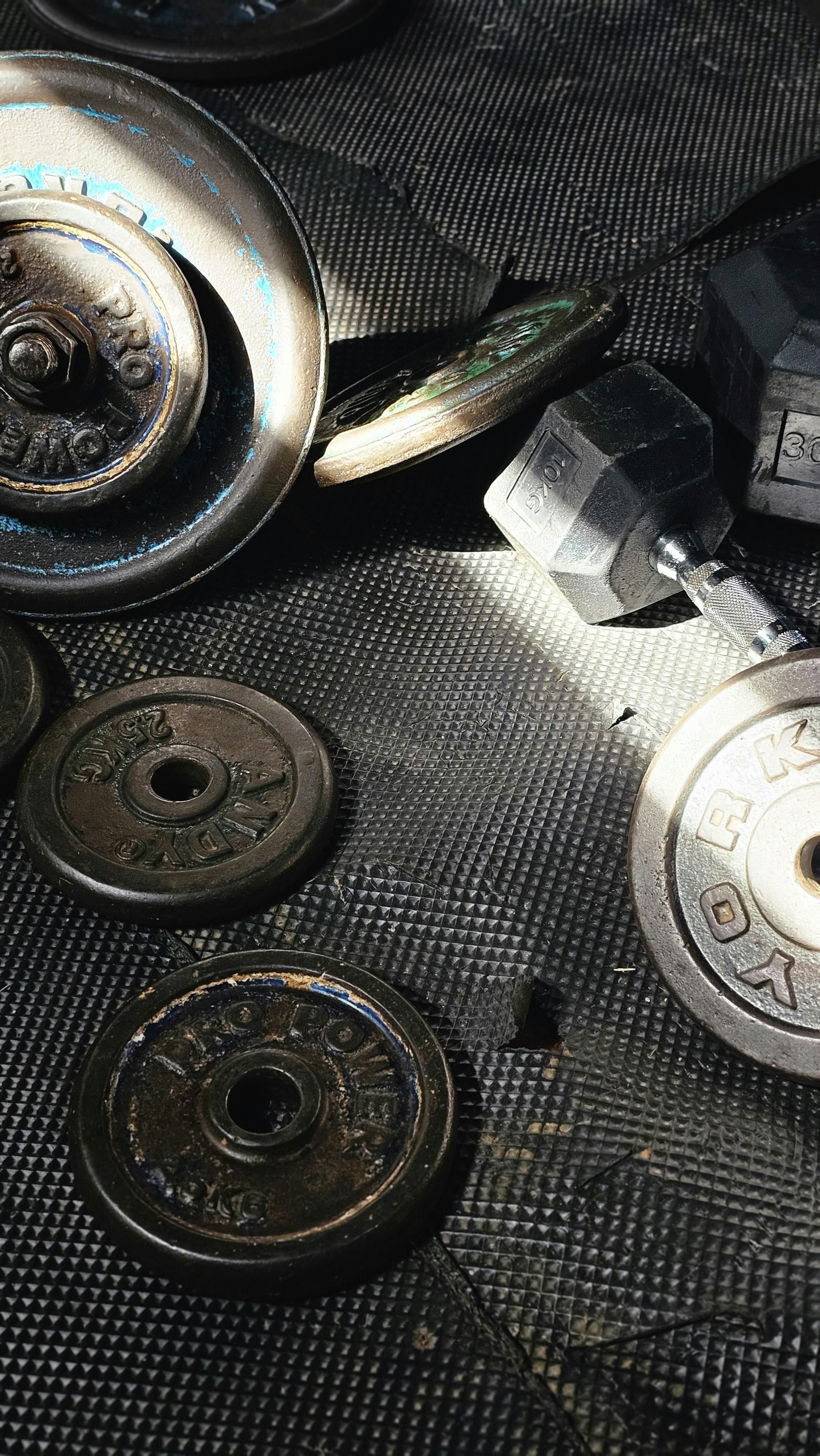 A collection of vintage weight plates and dumbbells on a textured gym floor highlighting fitness.