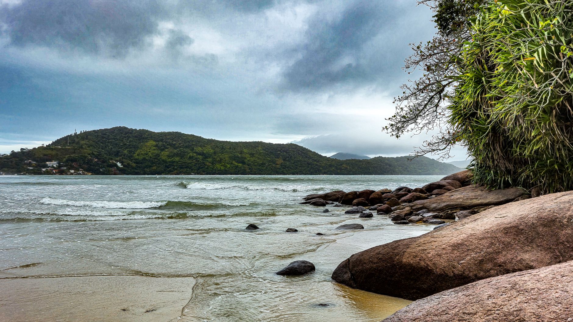 Peaceful beach scene at Praia da Enseada, São Paulo, Brazil, showing calm waters and lush hills.