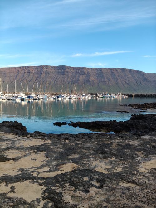 Free Tranquil harbor scene with sailboats under clear skies, set against a backdrop of majestic mountains. Stock Photo