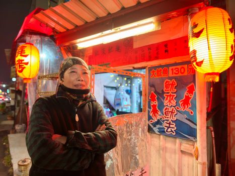 Night scene at a street food stall with a vendor and vibrant lanterns.
