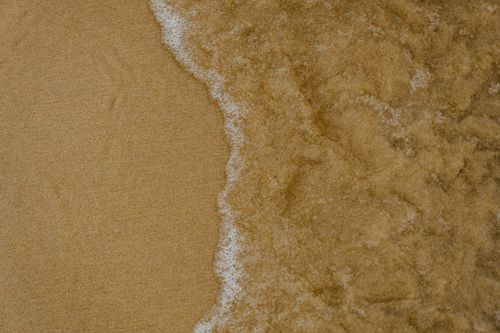Free Tranquil image of a gentle wave washing over golden sand on a peaceful beach. Stock Photo
