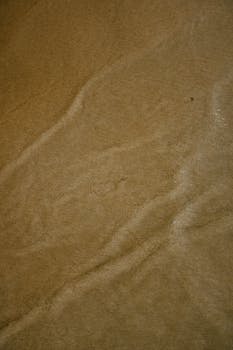 Close-up of sandy beach texture showing wave patterns, evoking a calm and natural feel.