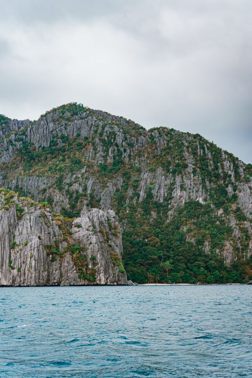 Free Stunning view of limestone cliffs with lush greenery by a calm sea under overcast skies. Stock Photo