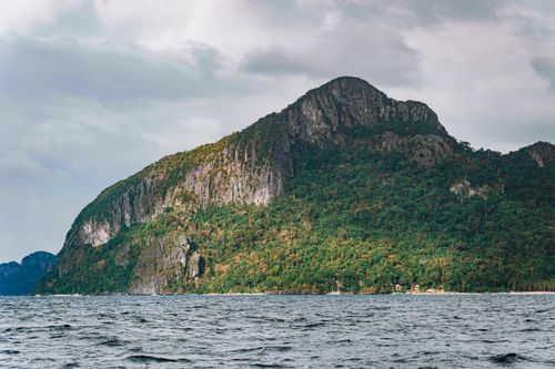 Free Stunning mountain island with lush greenery viewed from the sea under cloudy skies. Stock Photo