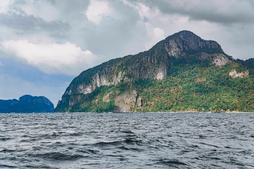 Free Dramatic and serene landscape of a lush mountain by the ocean under a cloudy sky. Stock Photo