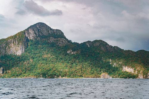 Free Scenic view of a lush green mountain by the sea under a cloudy sky, perfect for nature and travel themes. Stock Photo