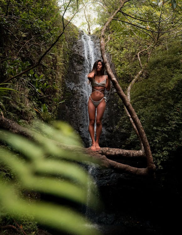 Mujer Vistiendo Bikini Gris De Pie En La Rama De Un árbol Frente A Cascadas Cerca De árboles Durante El Día