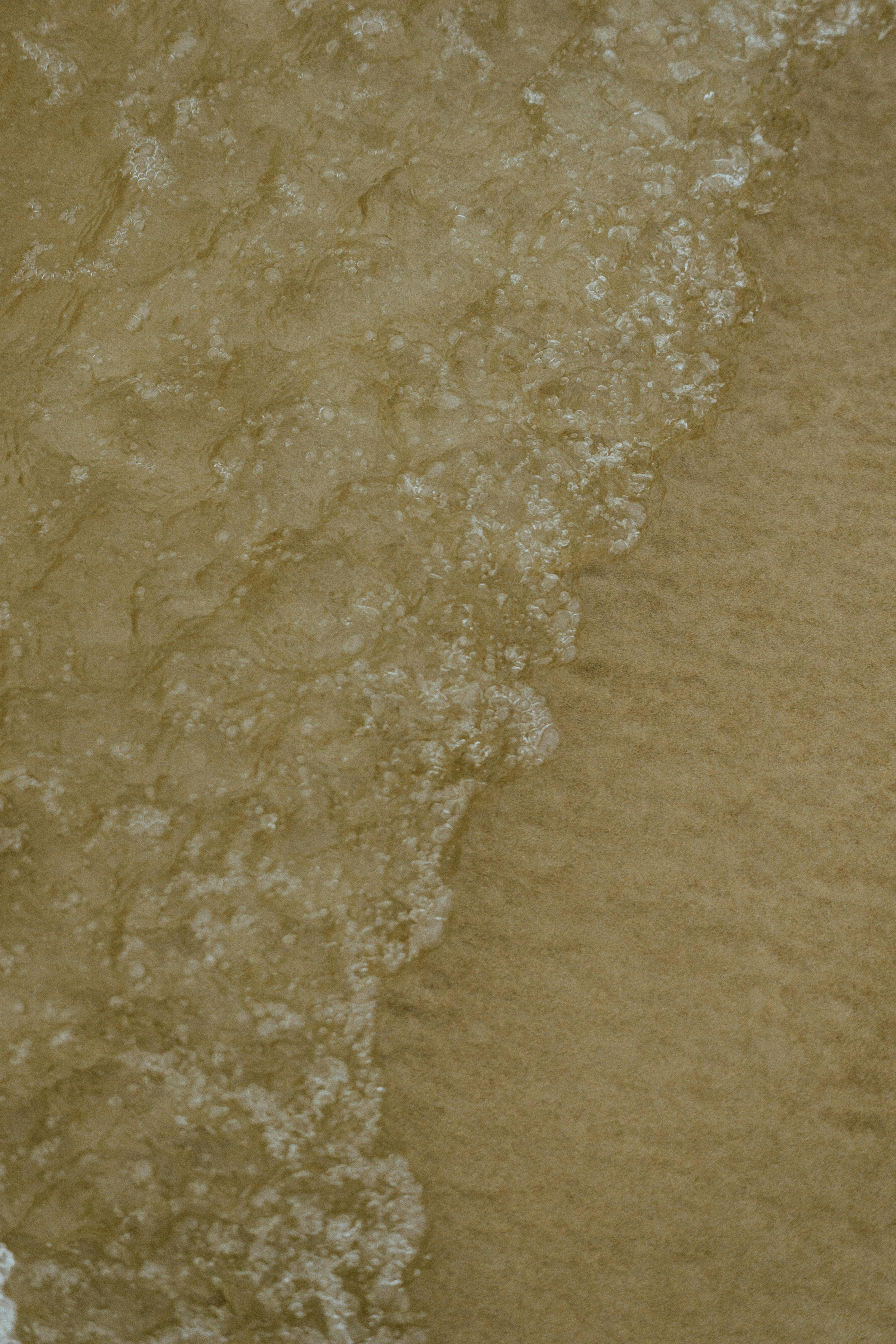 grátis Uma visão detalhada das ondas do oceano batendo suavemente na costa arenosa, criando uma textura relaxante. Foto profissional