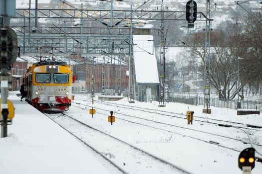 A yellow train arriving at Jönköping station, Sweden, surrounded by winter snow.
