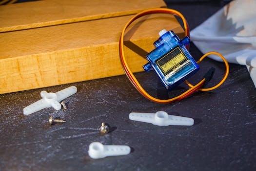 Close-up of a micro servo motor with plastic arms and screws on a workbench, ideal for robotics projects.