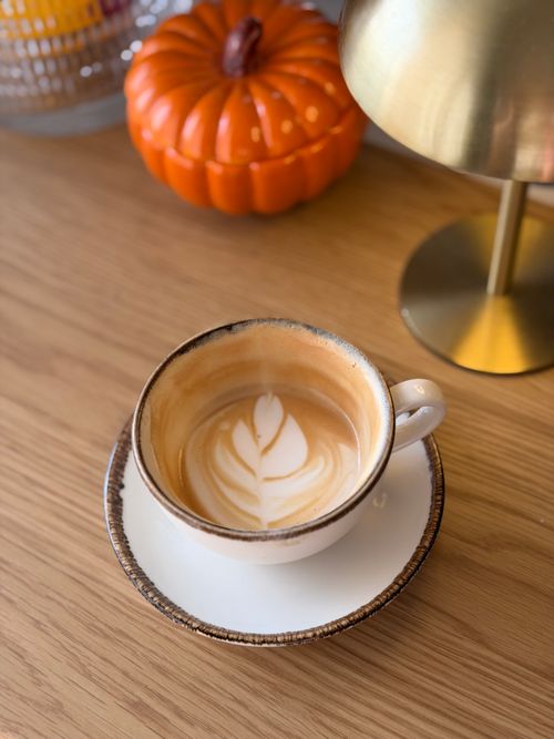 Free Warm latte with leaf art, pumpkin decor, and brass lamp on wooden table. Stock Photo