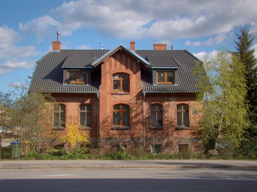 Free A picturesque red brick house with a slate roof, surrounded by trees, under a blue sky with fluffy clouds. Stock Photo