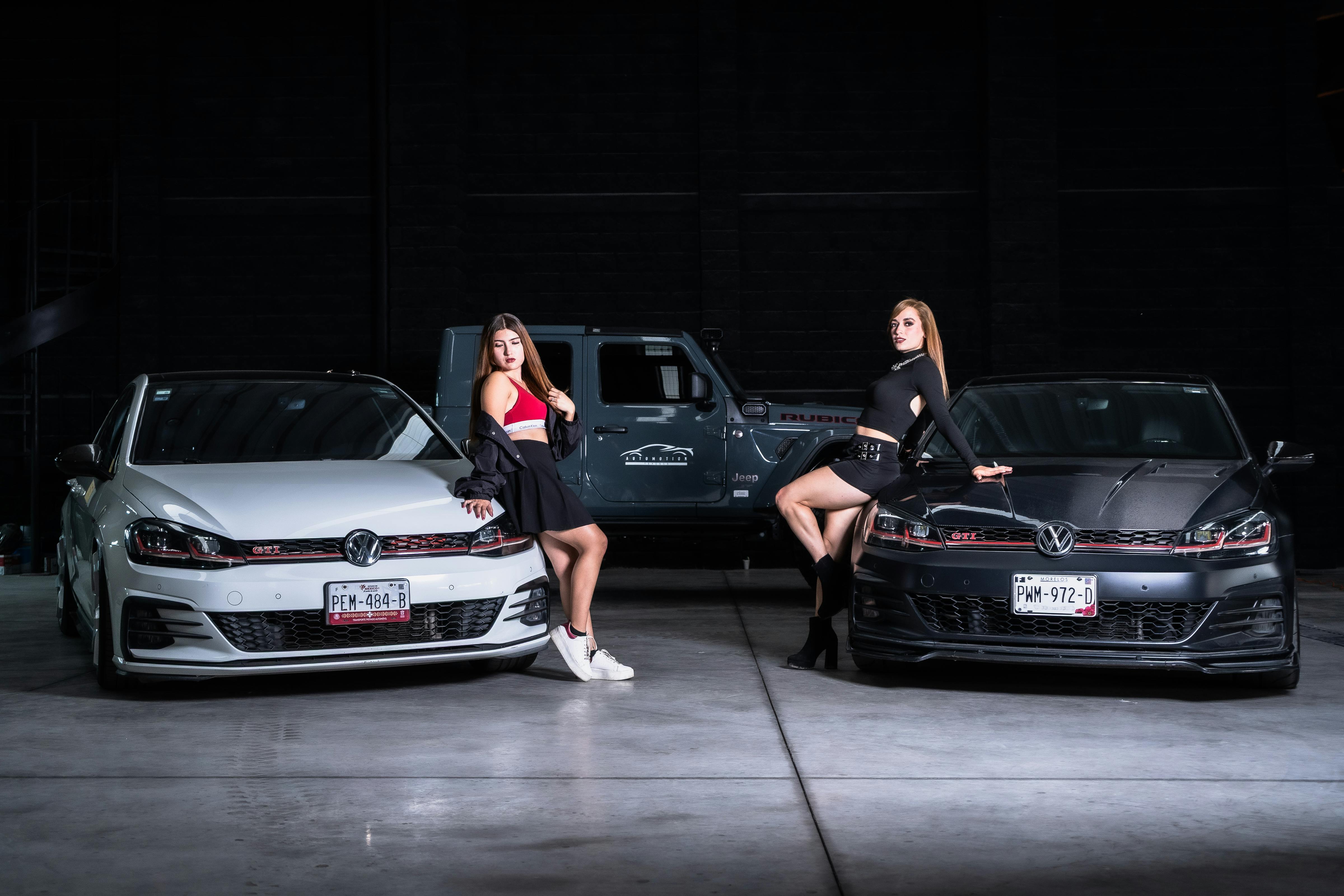 Zadarmo Dve ženy pózujú so športovými autami v interiéri a predvádzajú automobilový štýl. Fotka z fotobanky