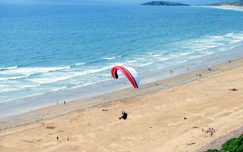 Free Aerial view of a paraglider soaring over a scenic beach in the UK, capturing coastal beauty. Stock Photo