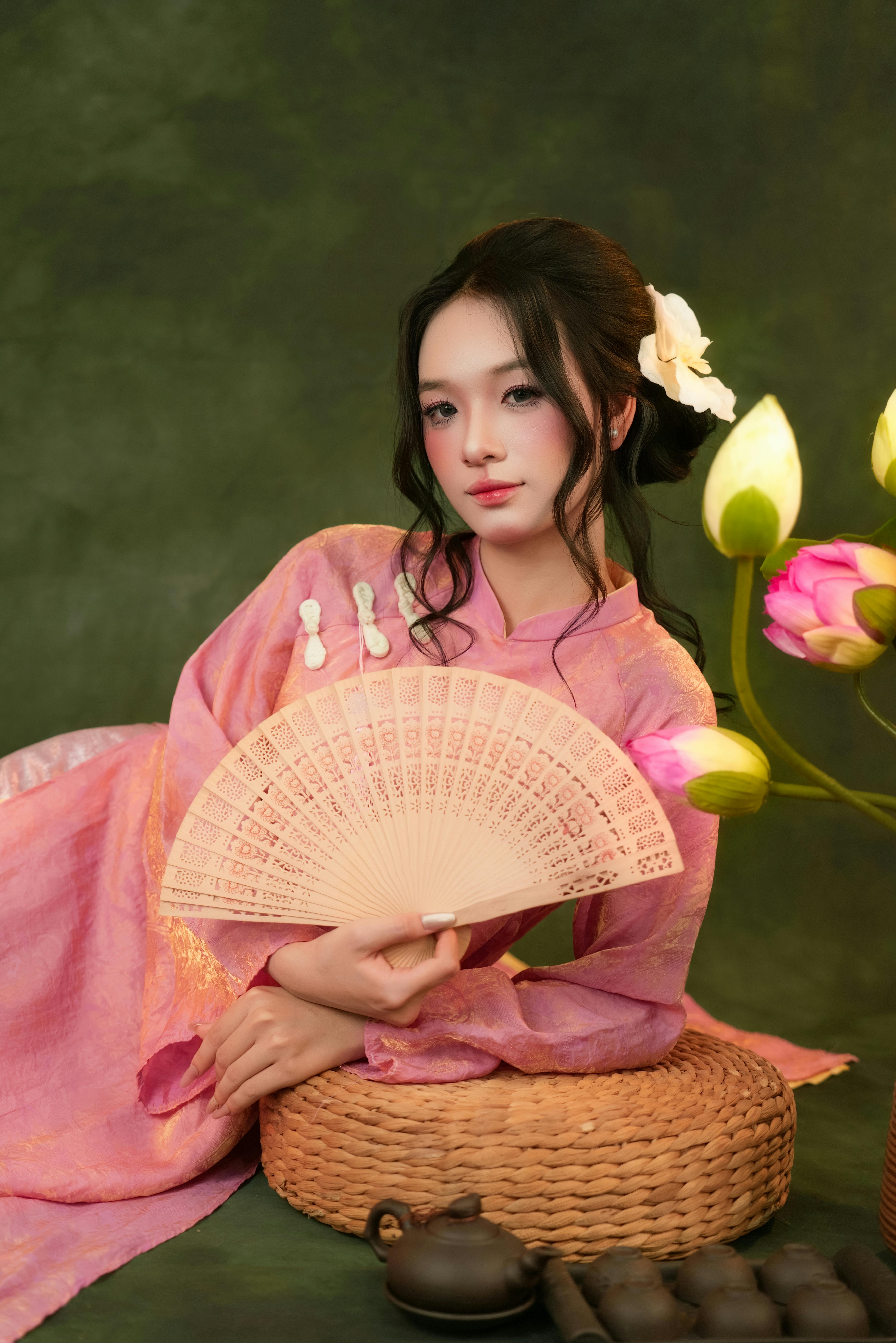 A woman in traditional attire gracefully holds a fan, surrounded by lotus flowers.