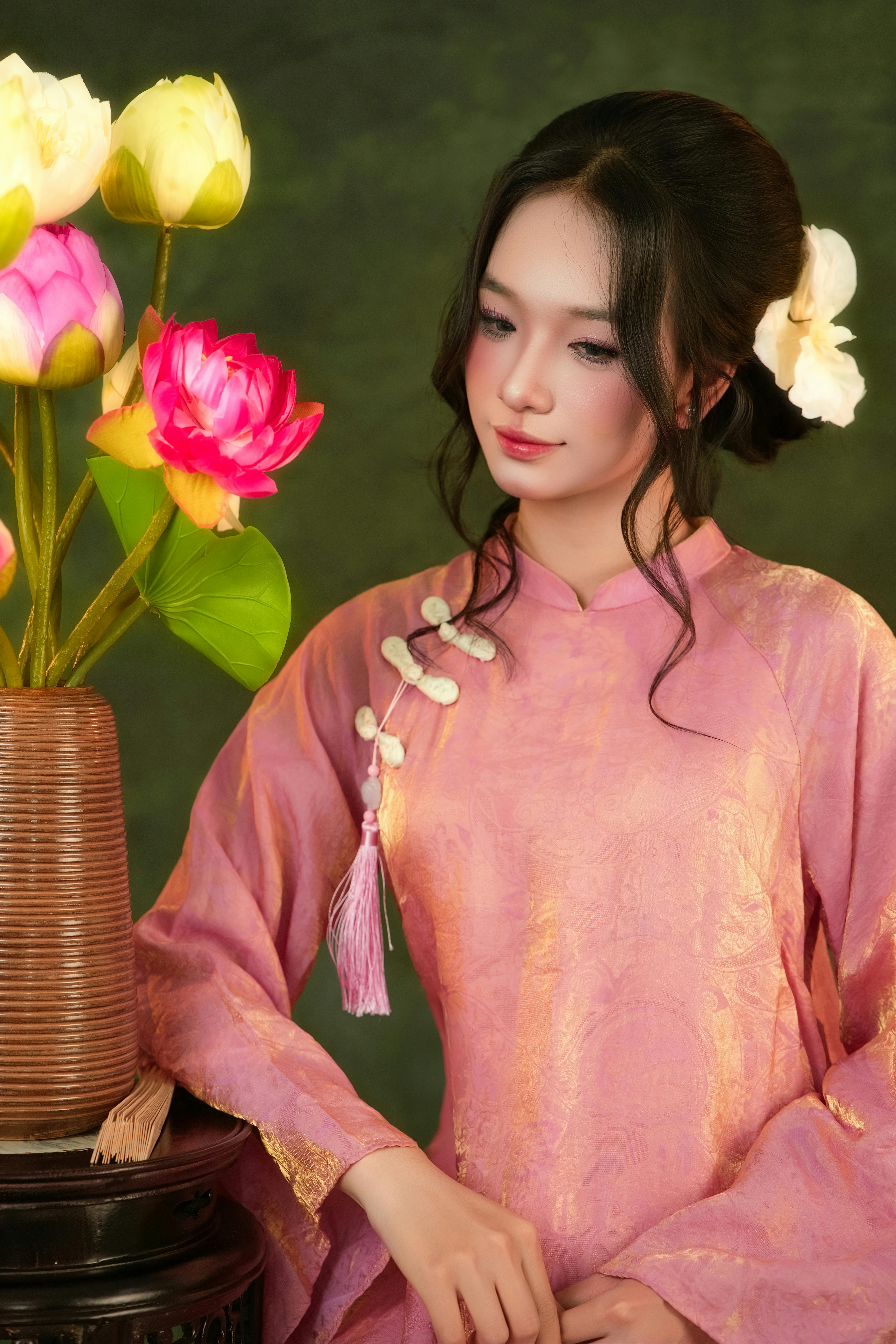 Young woman in pink ao dai with lotus flowers, capturing elegance and tradition indoors.