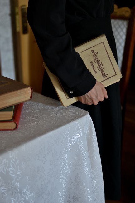 A person in black holds a vintage book near a lace-covered table.