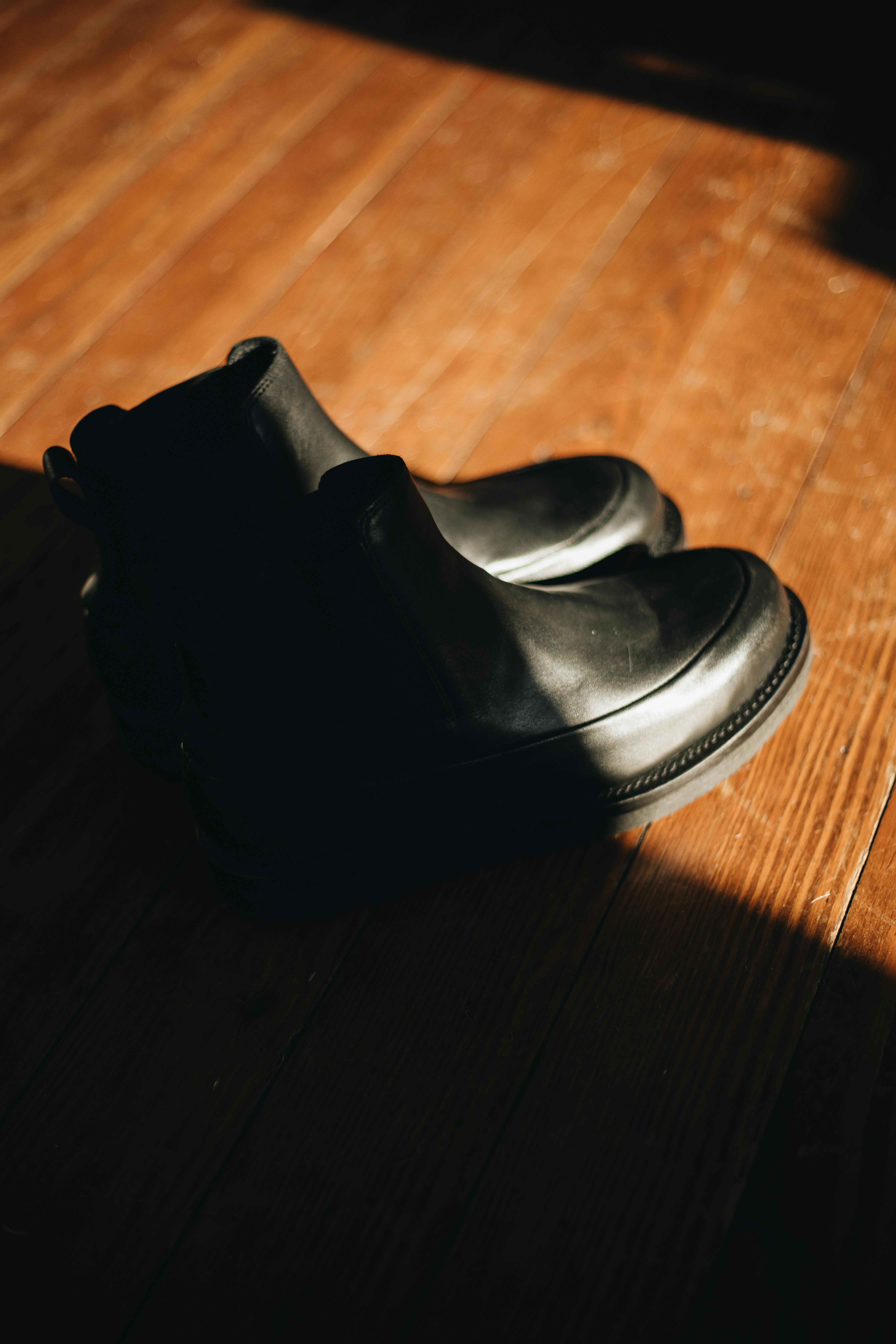 Kostnadsfria Klassiska svarta läderstövlar uppvisade med stämningsfull belysning på ett trägolv. Stock foto