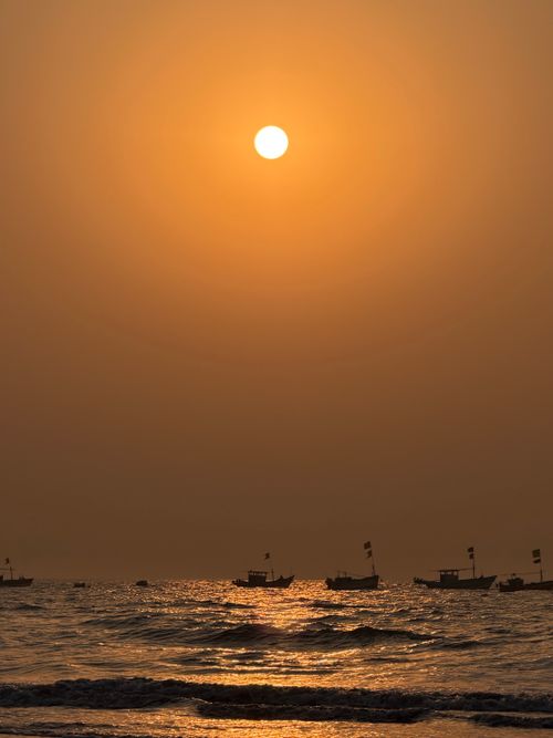 Free Peaceful sunset over a calm ocean with silhouetted boats. Tranquil and warm scene. Stock Photo