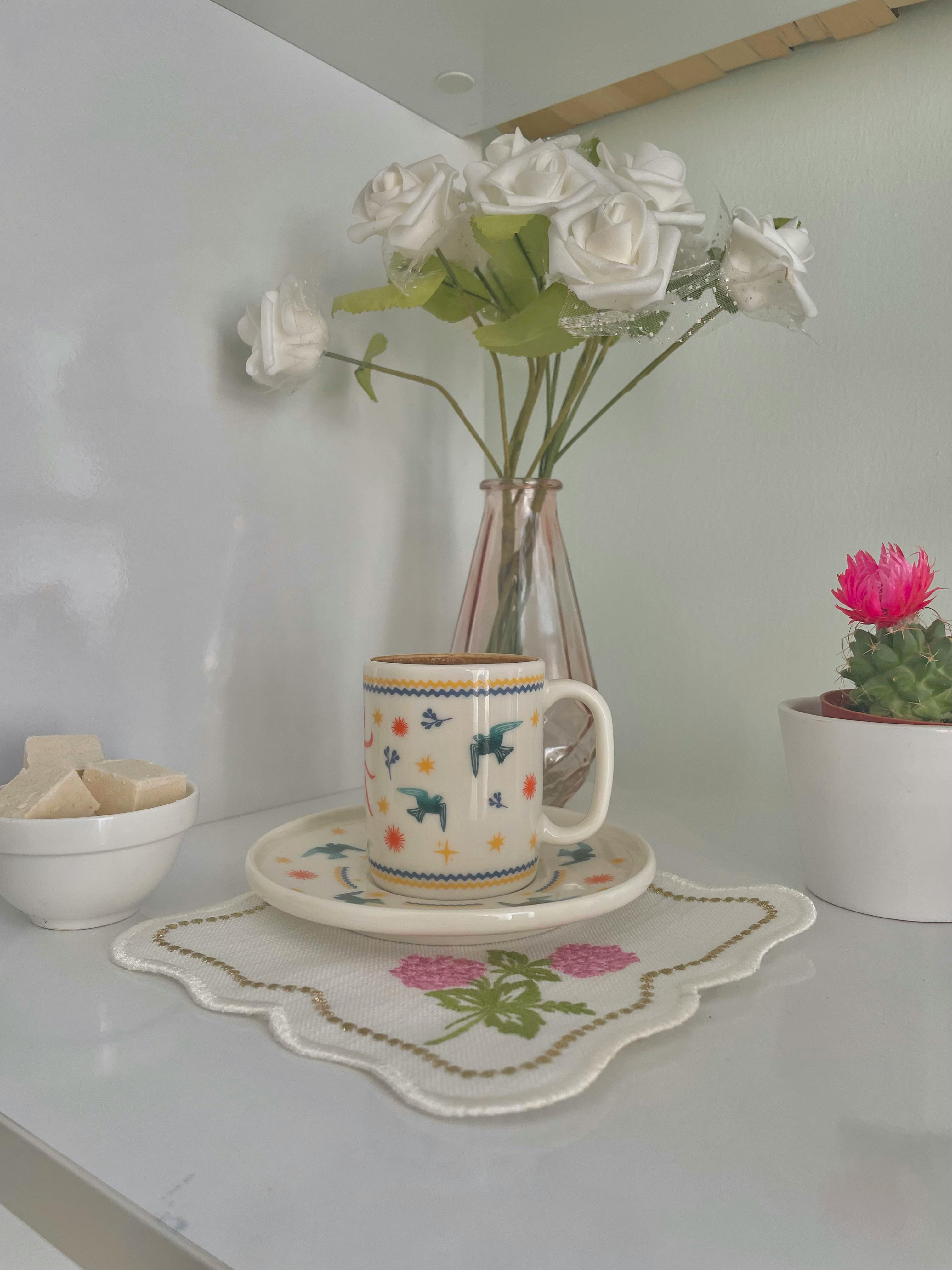 A cozy indoor tea setup with a floral mug, roses, and a cactus plant.