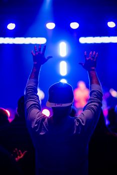 A vibrant scene of an audience member raising hands at a live concert with blue stage lights.