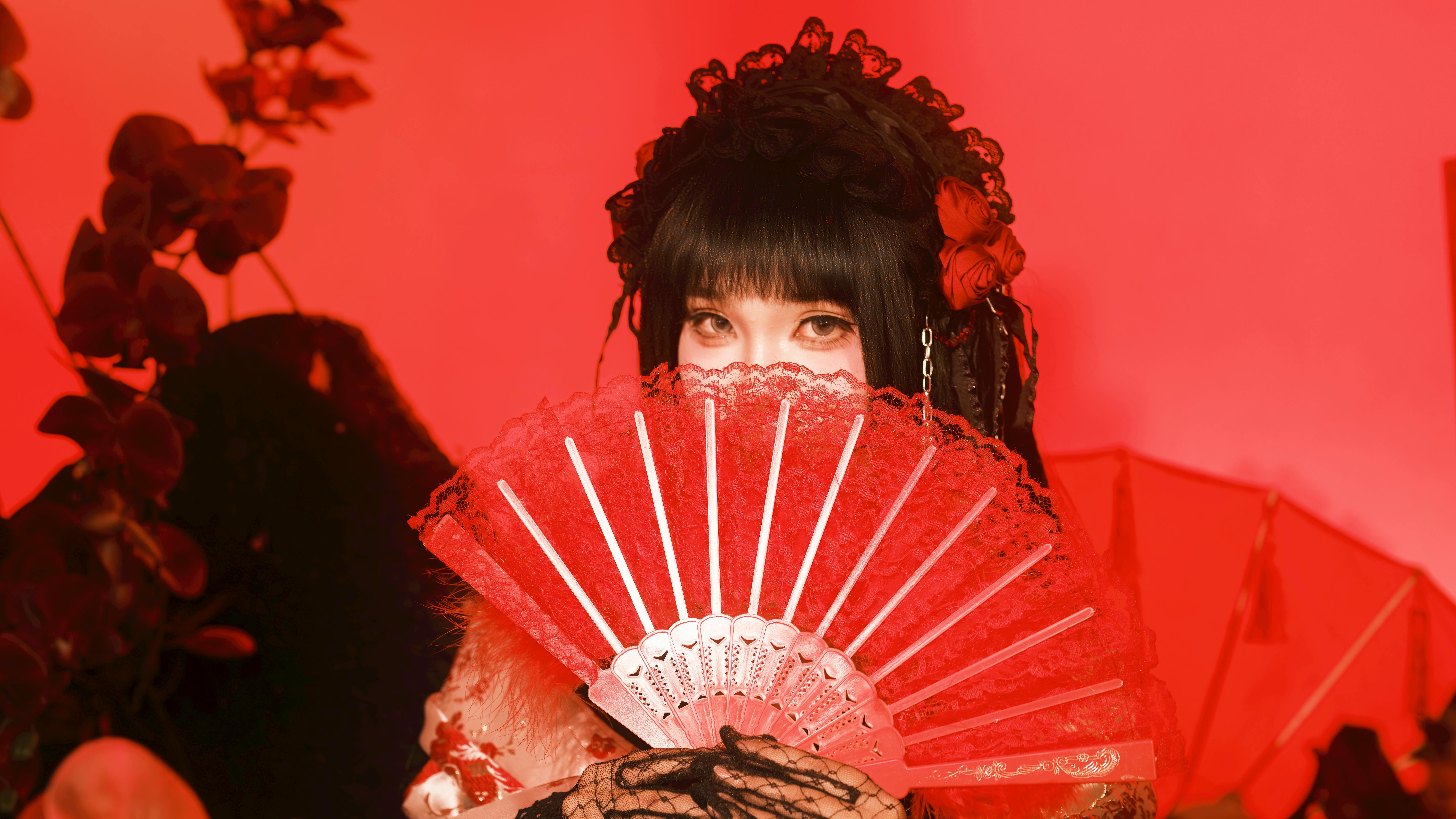 Mysterious portrait of an individual holding a red lace fan with vibrant red background.