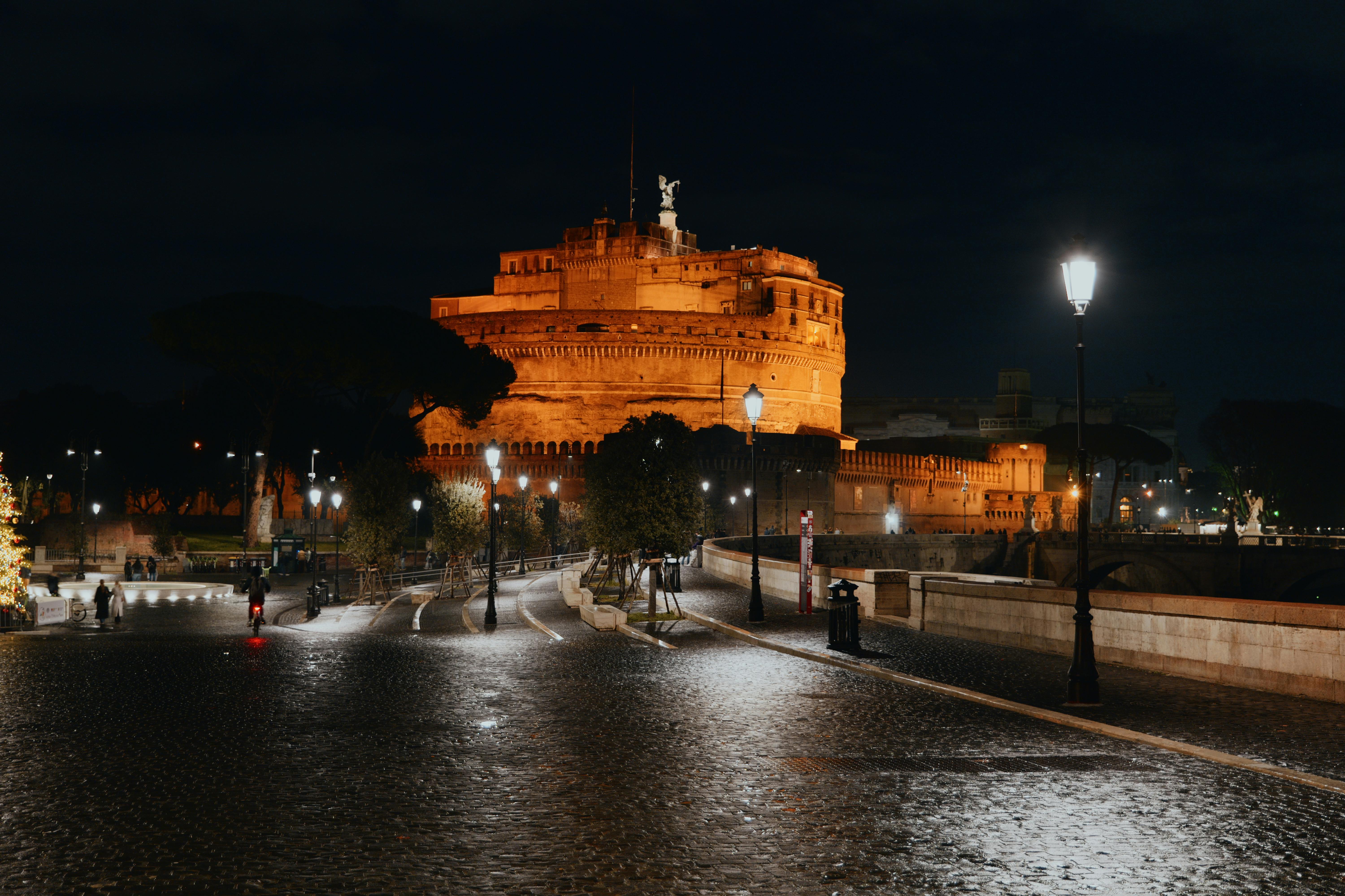 Beautiful nighttime capture of Castel Sant'Angelo in Rome, Italy, with streetlights illuminating the cobblestone path.