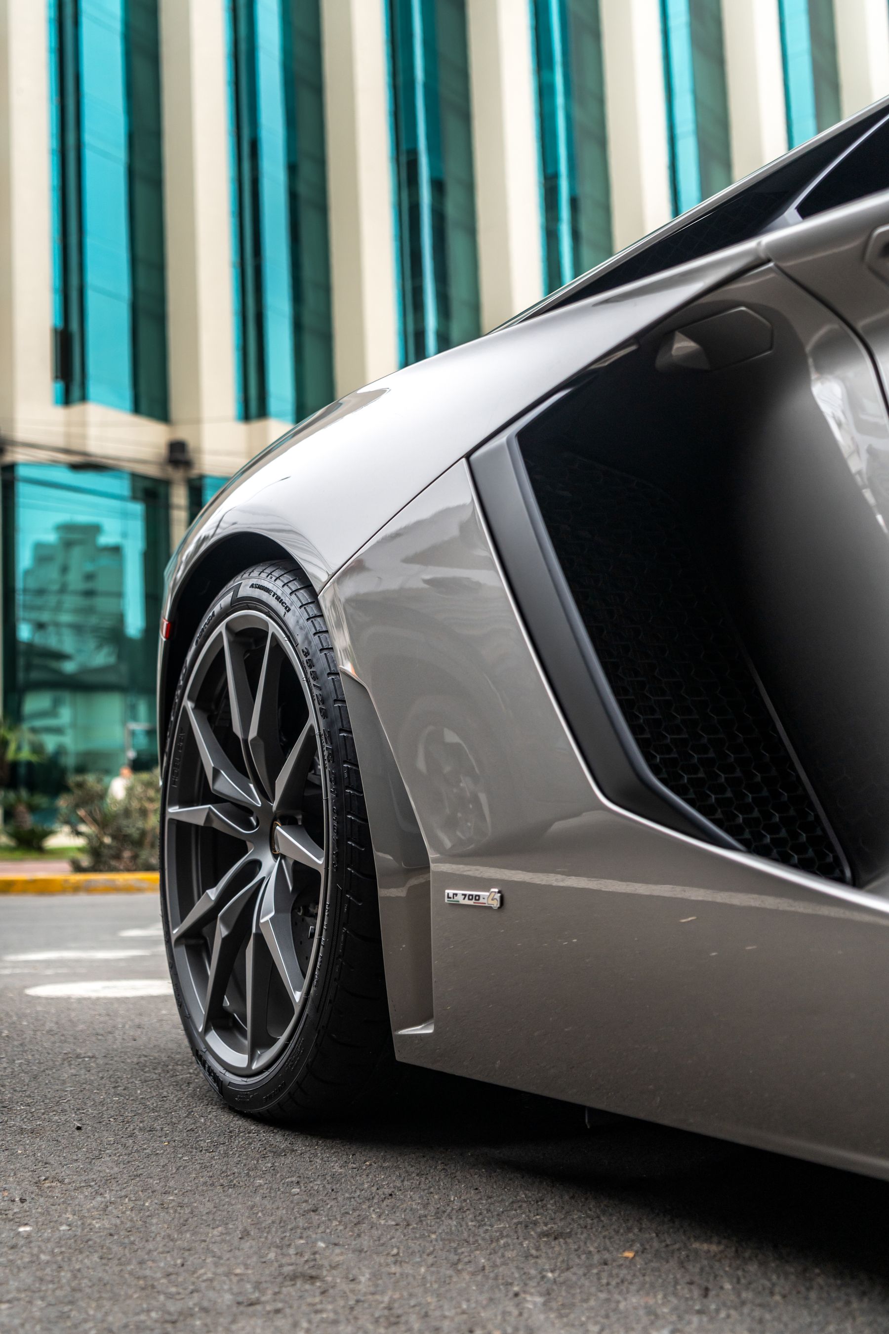 Close view of a silver performance car beside modern glass architecture