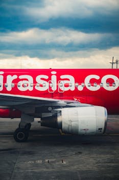 Close-up of a red airplane with visible logo at an airport runway under a cloudy sky.