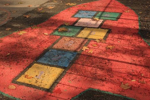 Colorful hopscotch court on playground with autumn leaves scattered around.