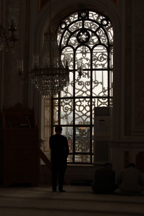 Free Silhouette of men praying inside an ornate mosque with a large decorative window in the background. Stock Photo