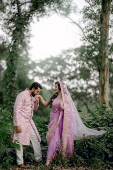 Couple in traditional Indian attire embracing in a lush forest setting.