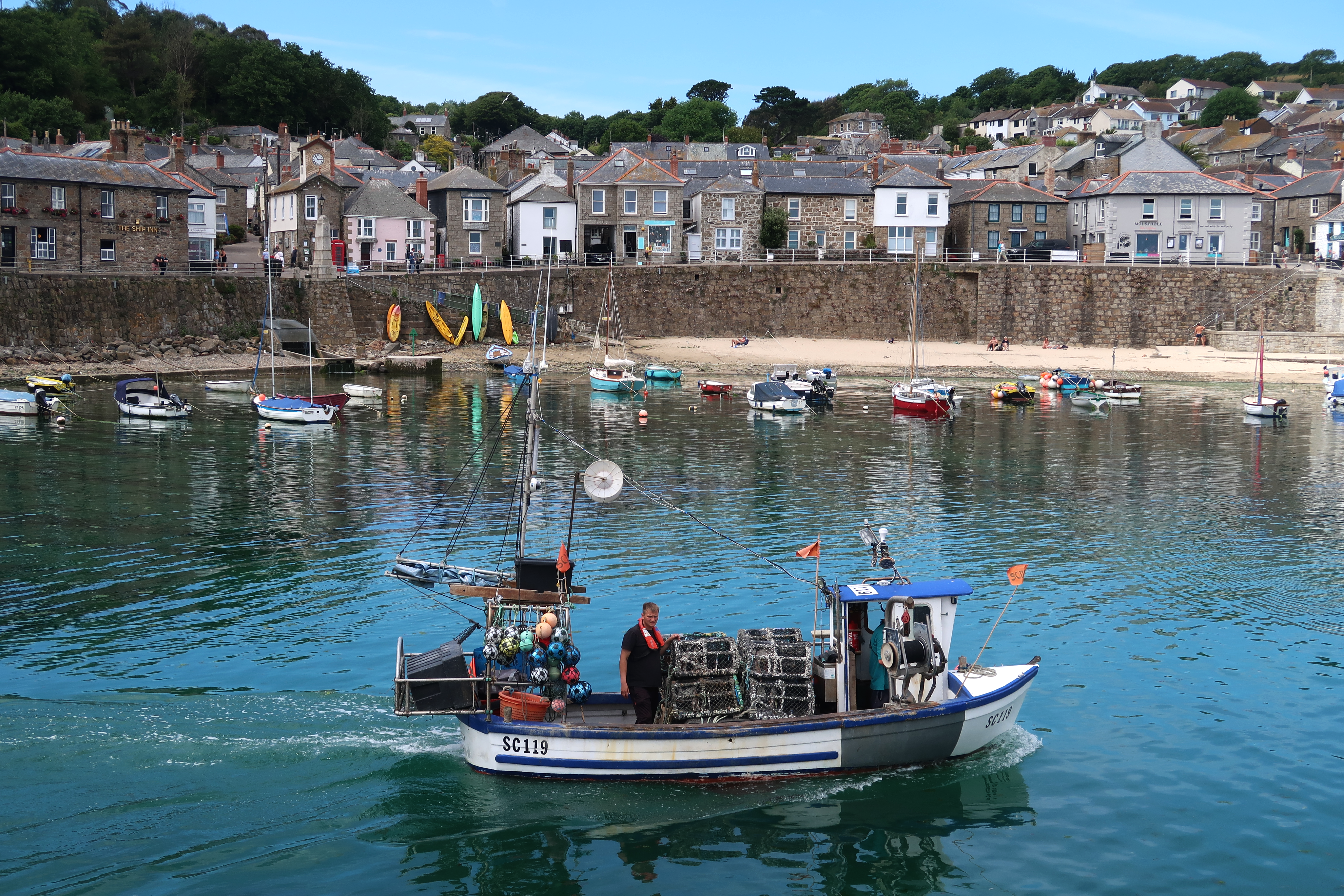 A lively scene of a fishing boat and historic harbor in Mousehole, England, showcasing seaside charm.
