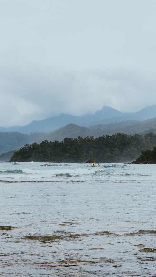 Free Serene seascape with a mountainous backdrop under a cloudy sky, ideal for travel inspiration. Stock Photo