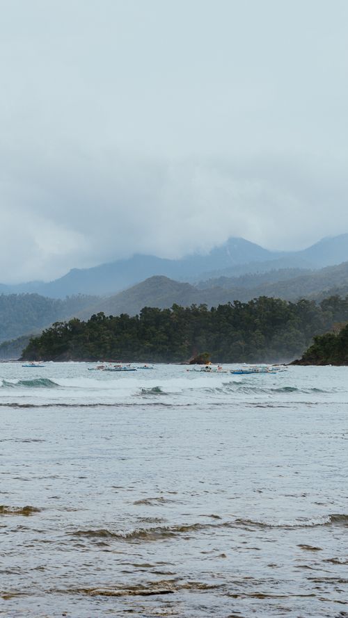Free Tranquil coastal view with mountains and cloudy skies reflecting serenity and peace. Stock Photo