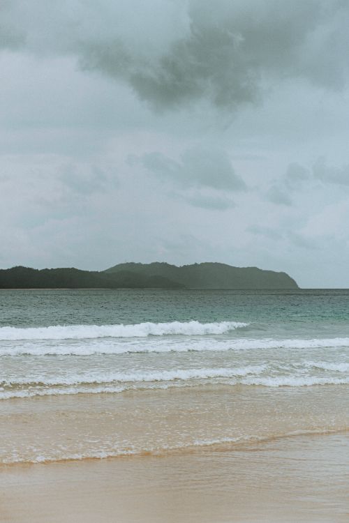 Free A tranquil view of a beach with gentle waves and an overcast sky. Stock Photo